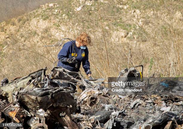 In this handout photo provided by the National Transportation Safety Board, an investigator works at the scene of the helicopter crash that killed...