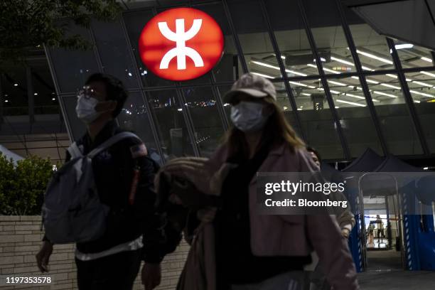 Passengers wearing protective masks pass an illuminated MTR Corp. Logo outside the West Kowloon Station in Hong Kong, China, on Wednesday, Jan. 29,...