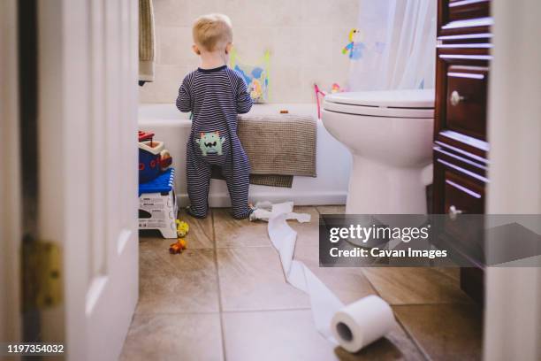 a baby boy stands in a bathroom with an unfurled toilet roll. - childrens closet stockfoto's en -beelden