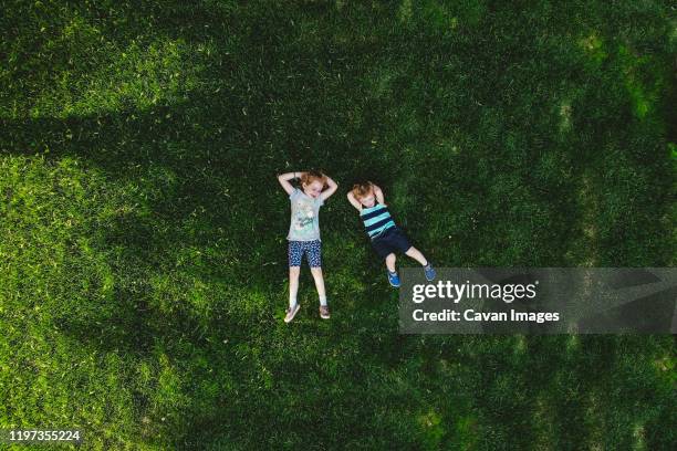 a drone shot of two children lying on a green lawn. - im gras liegen stock-fotos und bilder