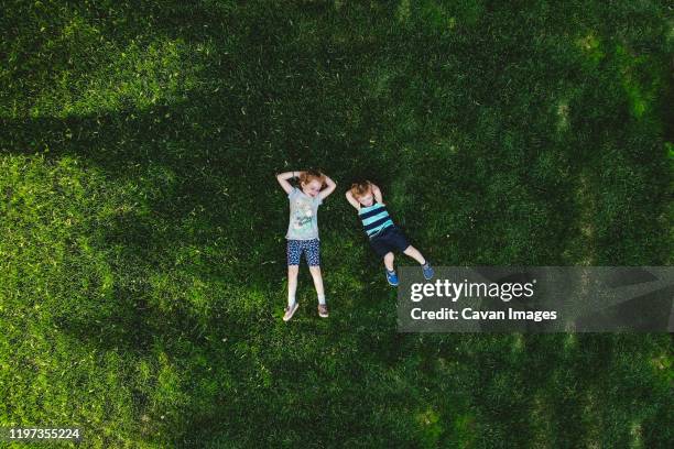 a drone shot of two children lying on a green lawn. - drone kid fotografías e imágenes de stock
