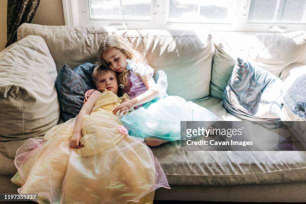 a boy and girl dressed in princess dresses sit on a couch. - stereotypical stock pictures, royalty-free photos & images