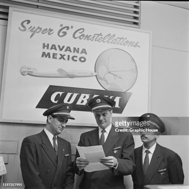 Three pilots of the Cubana de Aviacion SA airline under an advertisement for the Super G Lockheed Constellation, 1956.