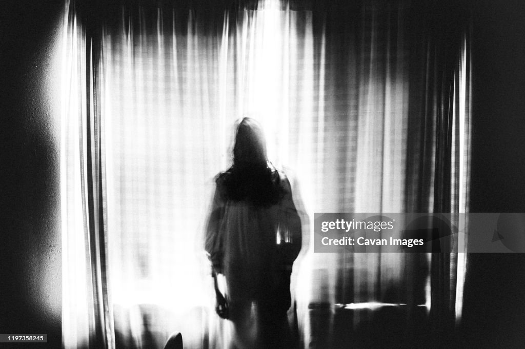 Spooky image of ghost girl standing in window in eery light