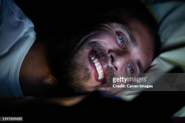 young man cannot sleep and is watching something on his phone - pick tooth photos et images de collection