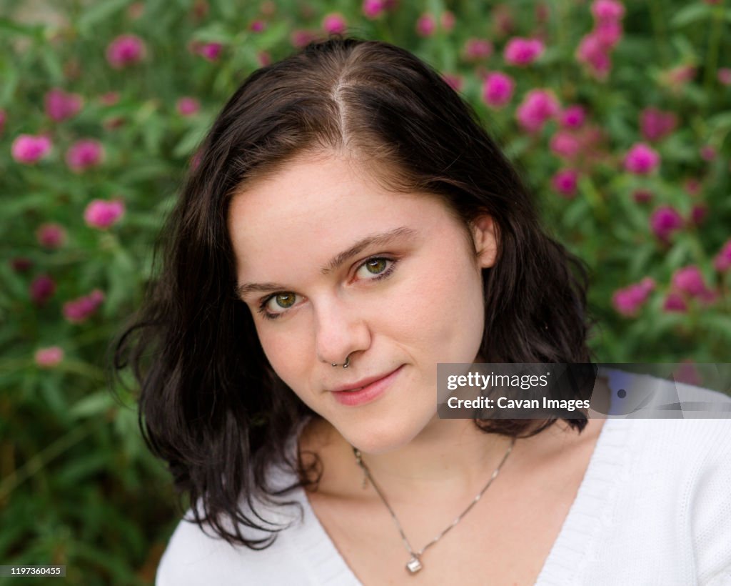 Portrait of a teenager with intense eyes and a nose ring by flowers