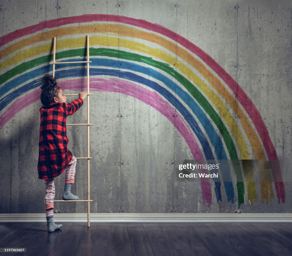 Meisje klimmen naar de regenboog te bereiken