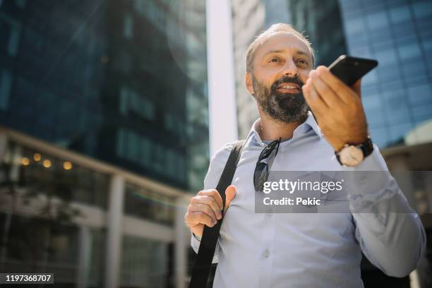 geschäftsmann sendet sprachnachricht beim verlassen des geschäftsgebäudes - übersetzung stock-fotos und bilder