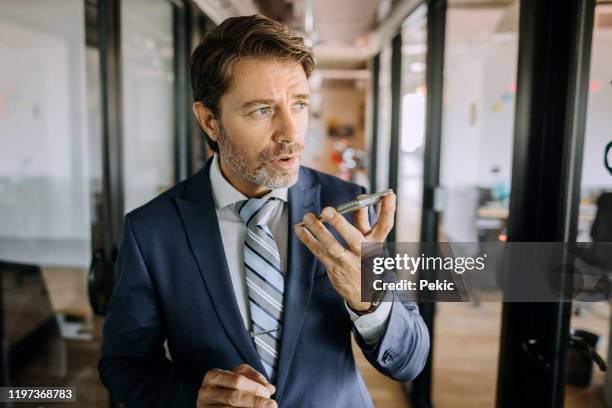 businessman in office sending voice message on his smart phone - voice command stock pictures, royalty-free photos & images