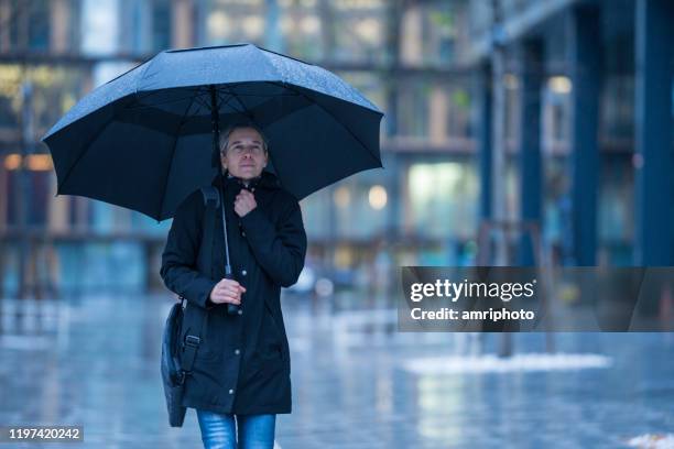 shivering woman with umbrella walking in rain through business office district in city - shivering shower stock pictures, royalty-free photos & images