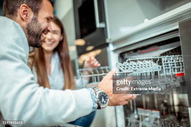 husband pulling out a dish tray out of a dishwasher with his wife by his side - buying washing machine stock pictures, royalty-free photos & images