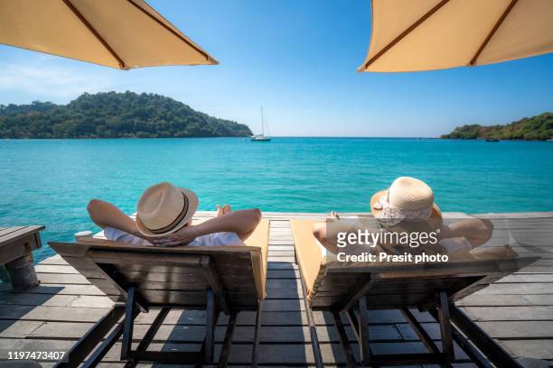 asian happy couple relaxing on chair beach with umbralla on wooden deck over sea background during summer vacation together in koh kood, trat, thailand. - man on the beach relaxing in deckchair fotografías e imágenes de stock