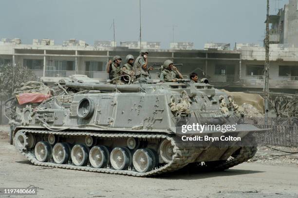 Israeli soldiers in an armoured vehicle pass destroyed houses on the streets of the Lebanese port city of Sidon during the Israeli army invasion...