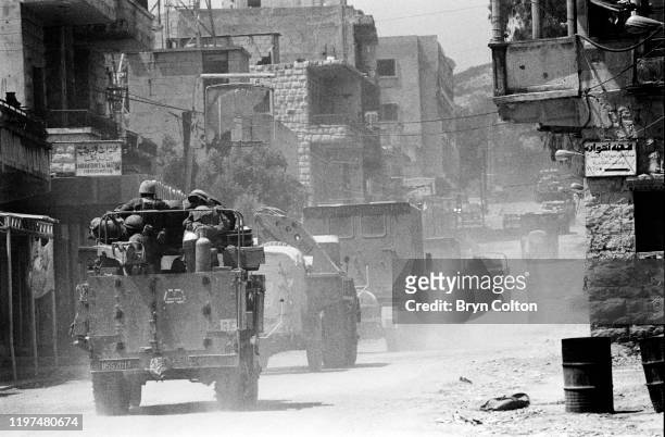 Israeli soldiers in armoured vehicles travel past houses as they pass through a village in the Bekaa Valley during the Israeli invasion of Lebanon,...
