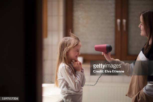 teenage girl using hairdryer to blow dry younger sister's long hair in a bathroom - fuel and power generation stock-fotos und bilder