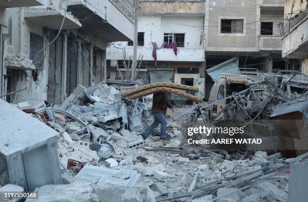 Man carries foam mattresses as he walks amidst the rubble and debris of a building at the site of reported airstrikes on the rebel-held town of Ariha...