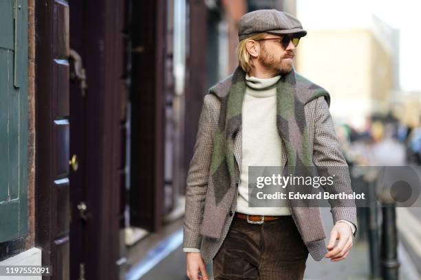 Alistair Guy wears a beret hat, sunglasses, a turtleneck pullover, a scarf, a blazer jacket, an orange belt, brown corduroy pants, suede shoes,...