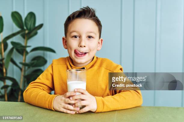 bambino carino di 6-7 anni che beve latte sul tavolo. sa che ha bisogno di bere latte per le ossa sane. adora il latte. - drinking milk foto e immagini stock