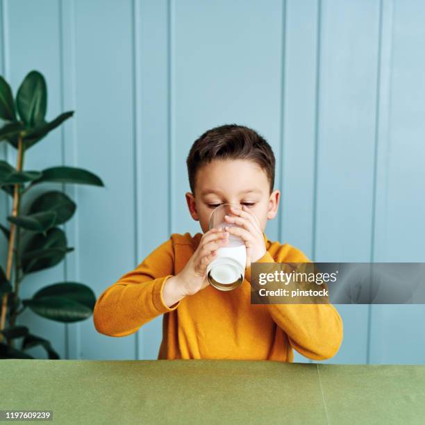 6-7 years old cute child drinking milk on table. he knows that he needs to drink milk for healthy bones. he loves milk. - boy drinking milk stock pictures, royalty-free photos & images