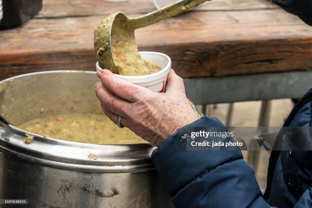 Elderly woman holding a plastic cup and fill it with Dutch green pea soup