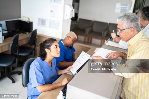 patient talking to a secretary at hospital reception - secretary stock pictures, royalty-free photos & images