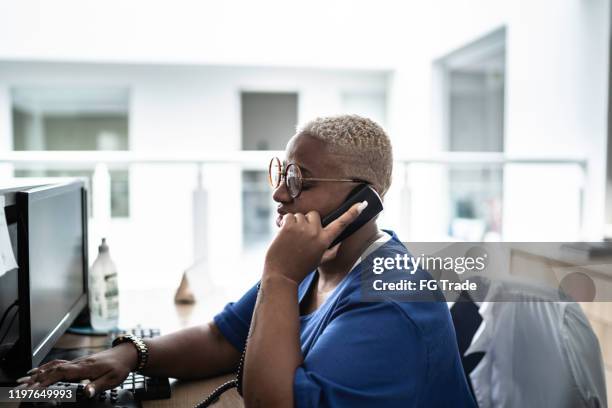 secretaris praten op telefoon bij ziekenhuis receptie - concierge stockfoto's en -beelden
