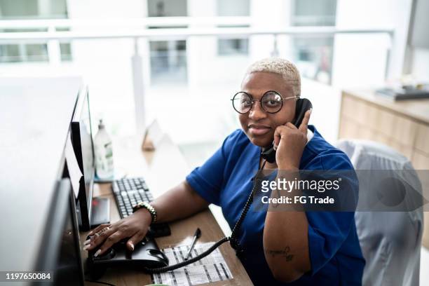 portrait of secretary talking on telephone at hospital reception - assistant imagens e fotografias de stock