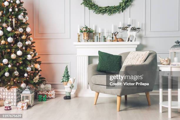 classic interior with an armchair tables, and a christmas tree with decorations on a light background of a wall with a fireplace. - christmas decorations stockfoto's en -beelden