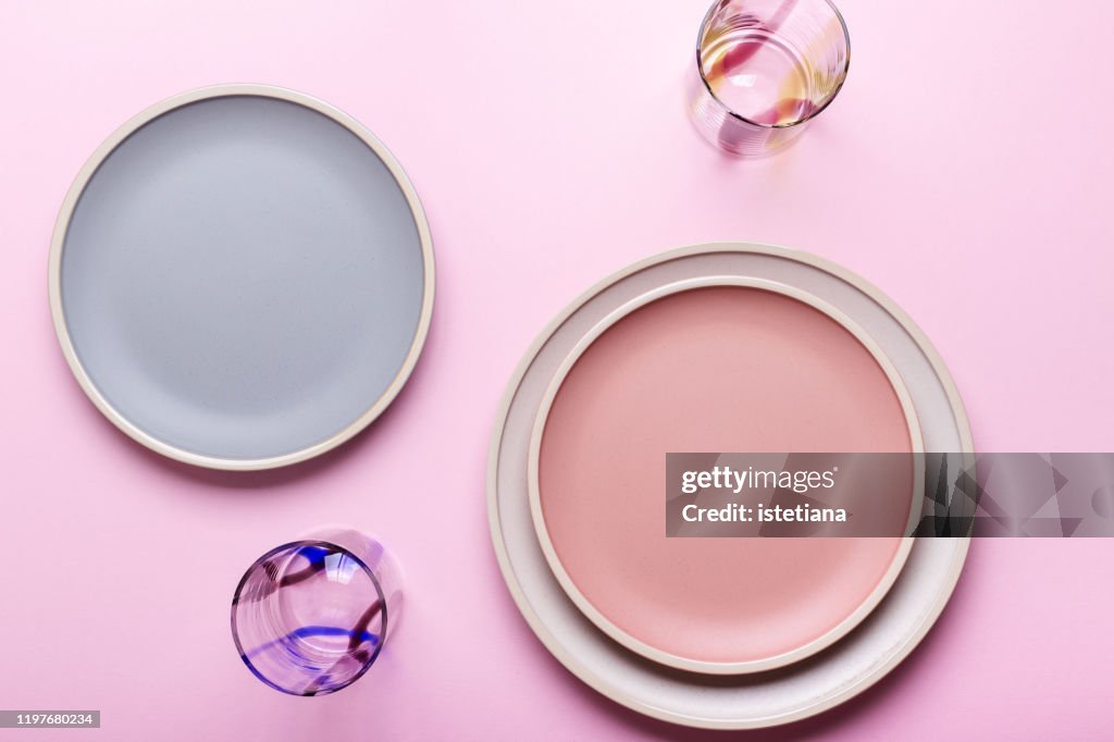 Empty plates and drinking glasses on pink background