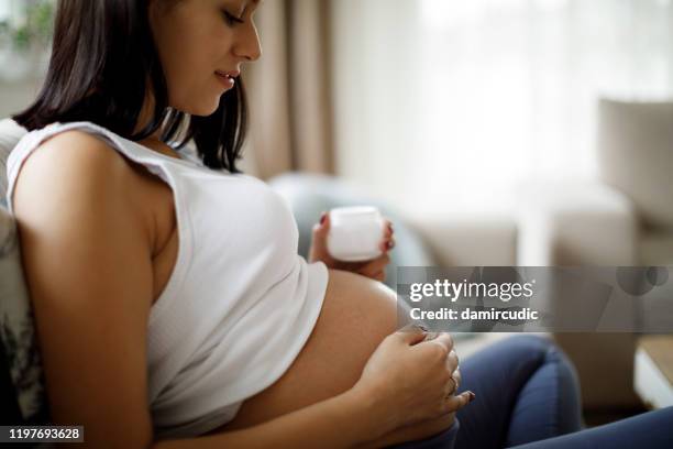 pregnant woman applying skincare cream on her belly to prevent stretch mark - mom resting stock pictures, royalty-free photos & images