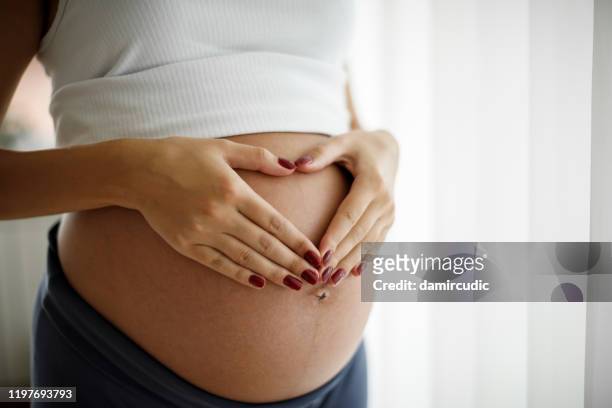 pregnant woman holding her belly and making a heart shape - abdomen stock pictures, royalty-free photos & images