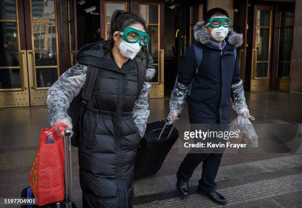 Chinese couple wear protective masks and goggles after getting off a train as they and others return after the Spring Festival holiday on January 31,...
