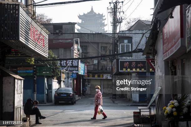 Woman wears a protective mask walk in the street as man sit in the roadside on January 31, 2020 in Wuhan, China. World Health Organization...