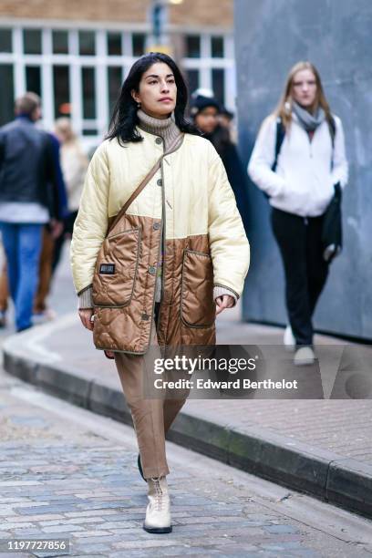 Caroline Issa wears a brown wool turtleneck pullover, a yellow and brown lustrous long puffer coat, pants, shoes, during London Fashion Week Men's...