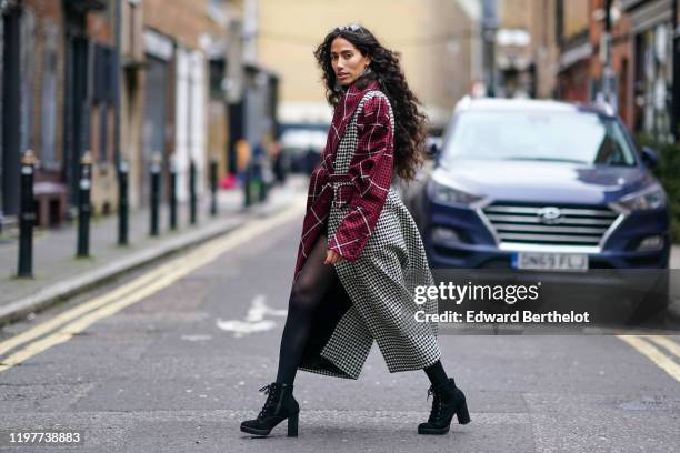 Artist Ciinderella B wears sunglasses, earrings, a red black and white houndstooth pattern print long trench coat, black shoes, during London Fashion...