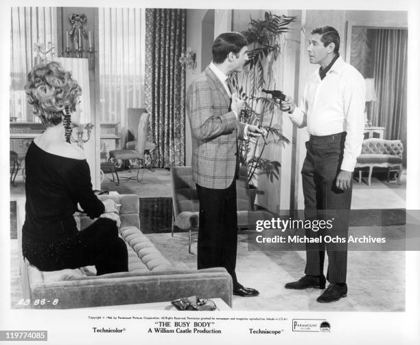 Anne Baxter sits while Sid Caesar has gun pointed at him by Jan Murray in a scene from the film 'The Busy Body', 1966.