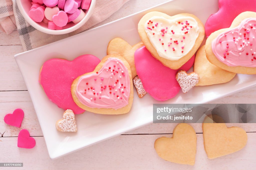 Heart shaped Valentines Day cookies with pink and white icing, overhead on a plate against white wood