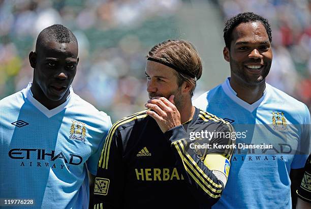 David Beckham of Los Angeles speaks with Mario Balotelli of Manchester City as teammate Joleon Lescott smiles while they pose for a team photo during...