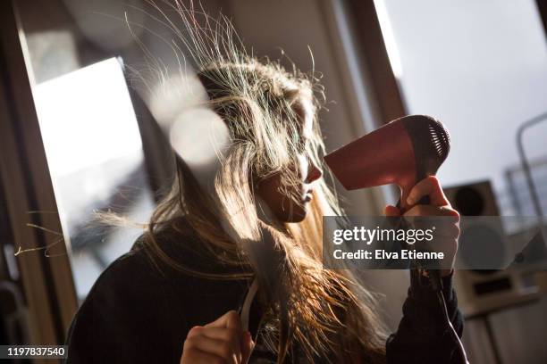 girl (12-13) blow drying her long hair with an electric hairdryer in a bedroom - haare föhnen stock-fotos und bilder
