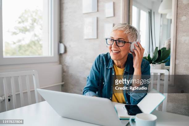 volwassen vrouw freelancing van haar thuiskantoor - luisteren stockfoto's en -beelden