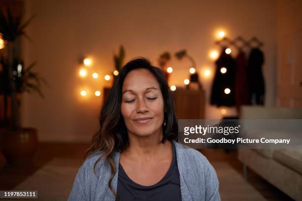 femme mûre sérénissime souriant tout en méditant à la maison - salle yoga photos et images de collection