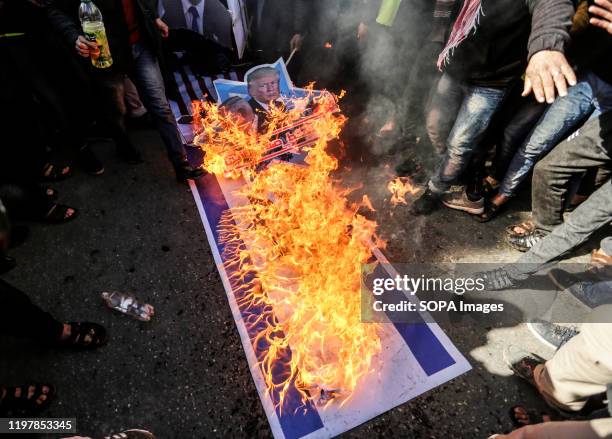 Palestinian demonstrators burn portraits of US President Donald Trump and Israeli Prime Minister Benjamin Netanyahu with the slogan in Arabic "Down...