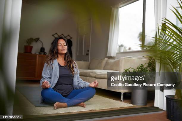 mature woman meditating while practicing yoga in her living room - zen stock pictures, royalty-free photos & images