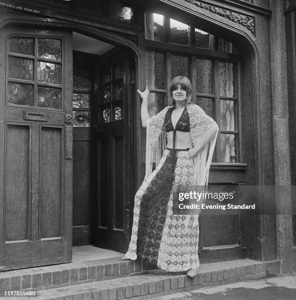 Female fashion model wears a crochet skirt with matching bra top and fringed shawl, designed by British fashion designer Thea Porter, in the doorway...