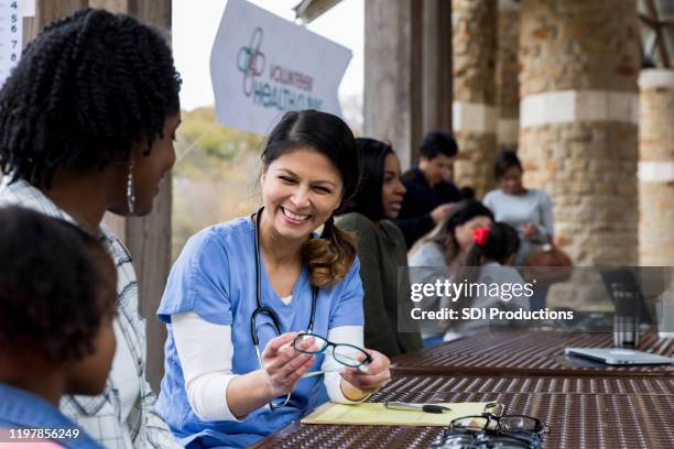 smiling mid adult optometrist offers glasses to young girl - altruismo stock pictures, royalty-free photos & images