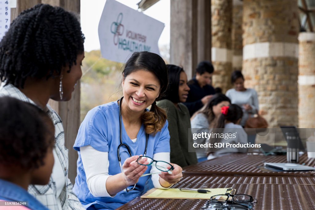 Smiling mid adult optometrist offers glasses to young girl