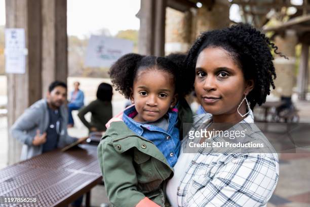 mid adult single mother holds young daughter at free clinic - serious stock pictures, royalty-free photos & images