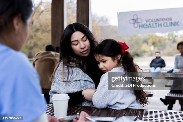 mother holds sick daughter at volunteer health clinic - worry free stock pictures, royalty-free photos & images