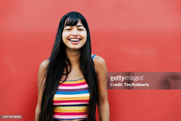 happy woman looking at camera, red wall - virginidad fotografías e imágenes de stock