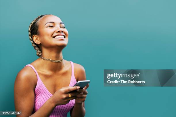 woman looking up with smart phone, blue wall - colour background cool portrait photography joy stock pictures, royalty-free photos & images